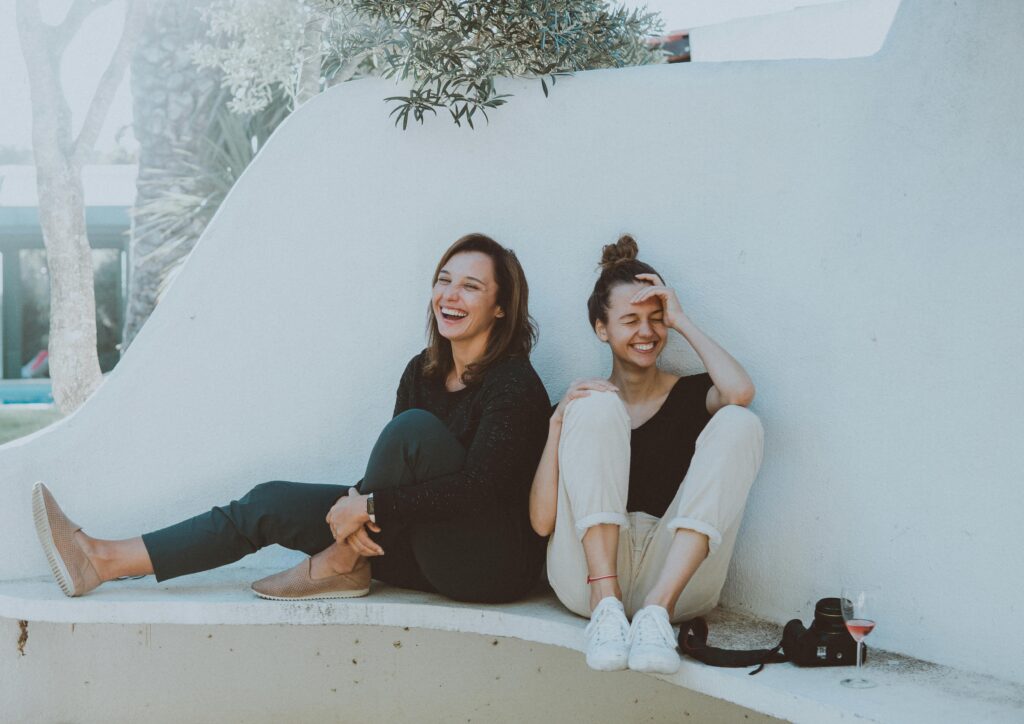 Two women sitting outdoors and laughing.